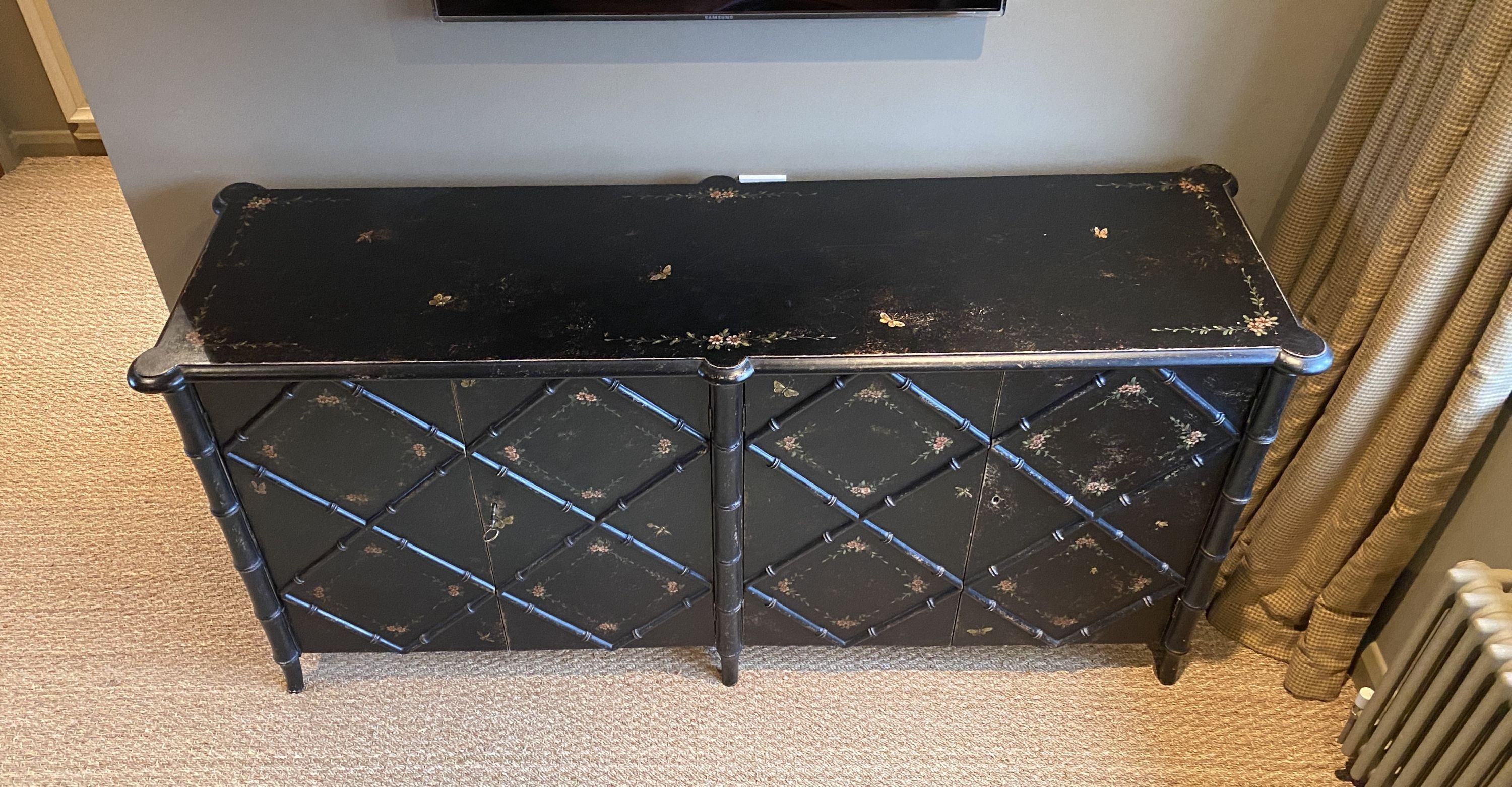 A black painted simulated bamboo low cabinet, with folding doors and floral painted decoration, width 180cm depth 55cm height 86cm, made to be used as a freestanding cupboard